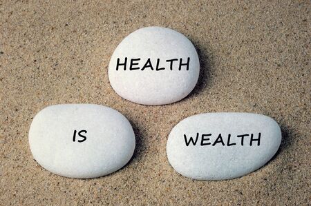 Health is wealth text on white zen stones on sand backgroundの写真素材