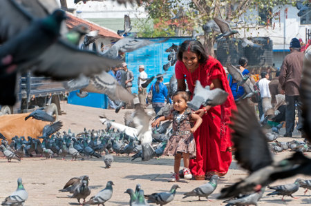 Kathmandu, Nepal - March 19, 2013: Woman in red sari with her daughter feeding a flock of pigeons at Patan Durbar square in Kathmandu Valley.のeditorial素材