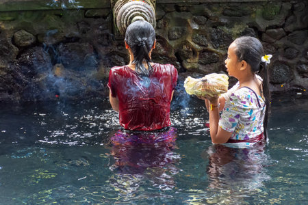 Gianyar, Indonesia - September 17, 2018: Unidentified woman praying and doing purification ritual at the holy spring water at Pura Tirta Empul temple.のeditorial素材