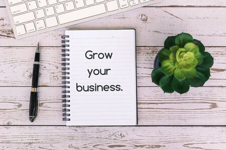 Grow your business text on notepad on top of wooden table, with computer keyboard, pen and potted plantの写真素材
