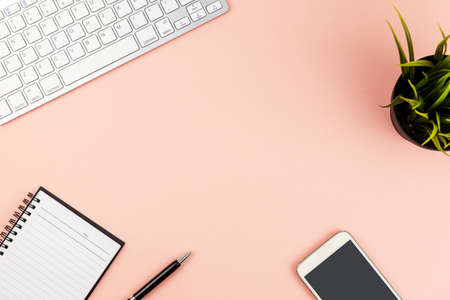 Flat lay office desk with computer keyboard, smart phone, pen, note pad and potted plant