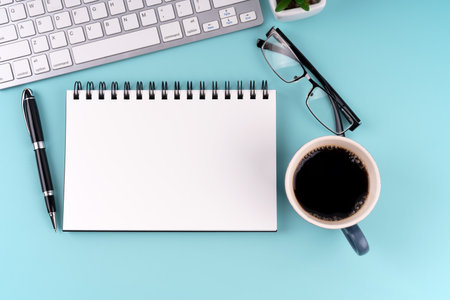 Blank notepad with cup of coffee and computer keyboard blue backgroundの写真素材
