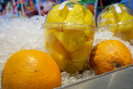 Fresh pineapple pieces in plastic transparent cups and oranges on ice for sale at farmers marketの写真素材