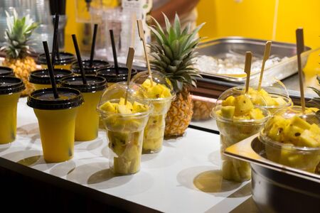 Fresh pineapple pieces and pineapple juice in plastic transparent cups for sale at street evening marketの写真素材
