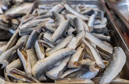A pile of fresh or frozen headless hake fish (merluccius) carcasses displayed in a stainless steel...