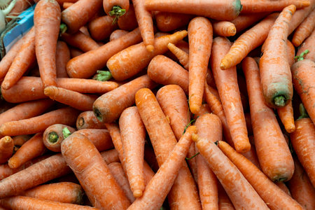 A dense pile of unwashed, fresh carrots with some green stems visible.