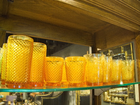 Orange colour glass cups on a wooden shelf in dinnerware shopの写真素材