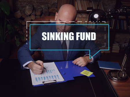 SINKING FUND text in block of quotes. Budget analyst doing paperwork A sinking fund is a fund containing money set aside or saved to pay off a debt or bond.の写真素材