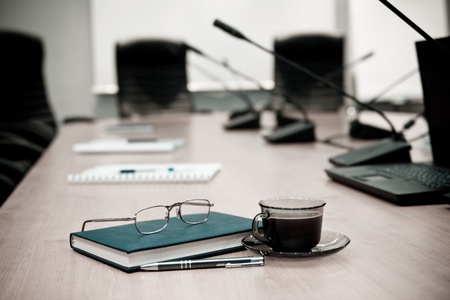 A close-up of a conference room showing a chairs, a table, a coffee cup,  and a note pad. Sharp focus on the cup.の写真素材