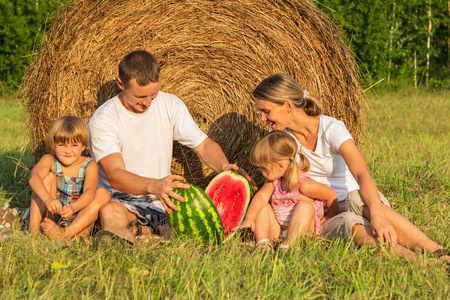 The family in the field with hay eats water-melon with two childrenの写真素材