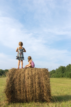 Two little sisters against the blue sky in summer day look from camera in distanceの写真素材