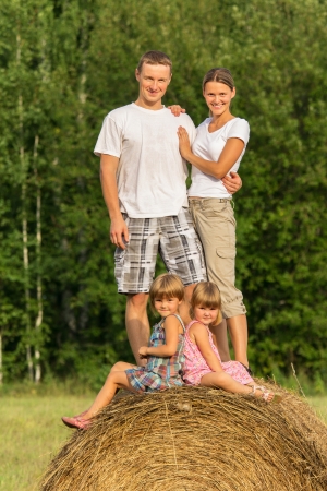 Happy family with two children on haystack in summer dayの写真素材