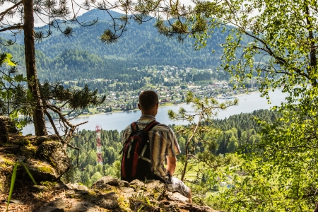 The young man sits and looks from above at the mountain lakeの写真素材