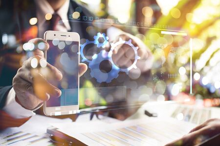 businessman holding a mobile phone with gear icon text on virtual screen concept.の写真素材