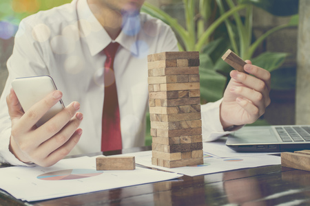 Young handsome businessman using wooden building blocks with white calculations scribbled around himの写真素材