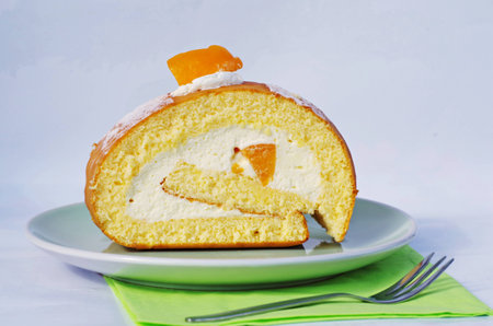 Delicious cake roll with peach and cream on plate with green napkin and fork on with background.の写真素材