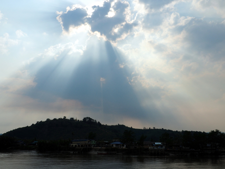 Light shines through the clouds at village river side near mountainの写真素材
