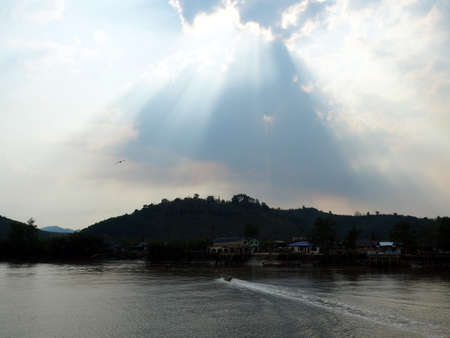 Light shines through the clouds at village river side near mountainの写真素材