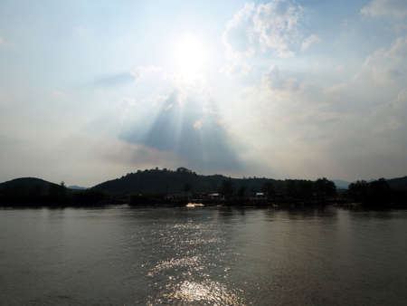 Light shines through the clouds at village river side near mountainの写真素材