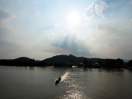 Light shines through the clouds at village river side near mountainの写真素材