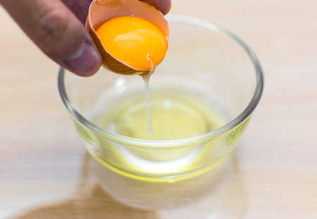 holding cracked egg over bowl on wood background.の写真素材