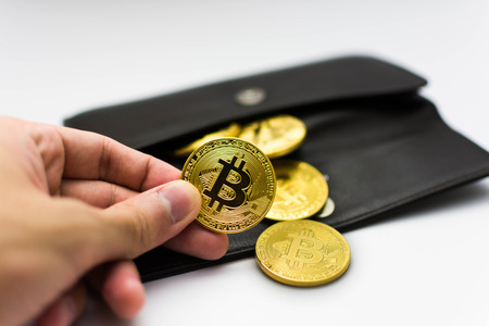 Golden bitcoins in hand. Digital symbol of a new virtual currency on white background and black wallet.の写真素材