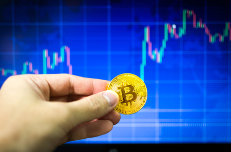 Man holding gold bitcoin and BTC trading chart in background, Financial conceptの写真素材