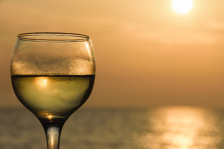 Side Angle View Of Glass Filled With White Wine Against Sea During Sunsetの写真素材