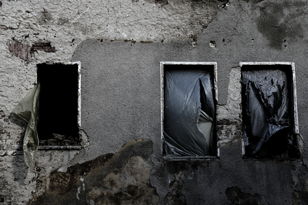 Scenic View Of Creepy Abandoned House Facade With Three Windows Covered In Plastic Materialの写真素材