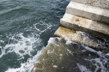 High Angle View Of Blue Sea With Splashing Waves Against Old Cement Stairs In Harborの写真素材