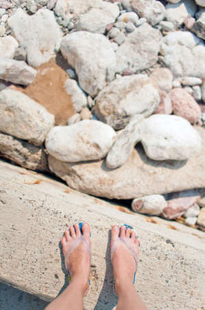 Overhead photo of feet on a background of big beach stones. Women feets view from above. Exploring, travelling, tourism, leisure.の写真素材
