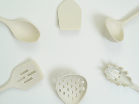 Flat lay of beige silicone kitchen utensils arranged in a circular pattern on a white background. Minimalist and stylish cooking tools ideal for modern culinary themes.の写真素材