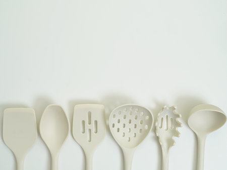 Set of beige silicone kitchen utensils neatly arranged in a row on a white background. Functional...
