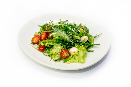 Salad of greens and cherry tomatoes on a plate on a white backgroundの写真素材