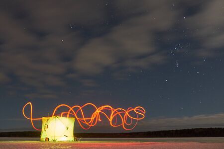 A tent for winter fishing at night stands on a lakeの写真素材