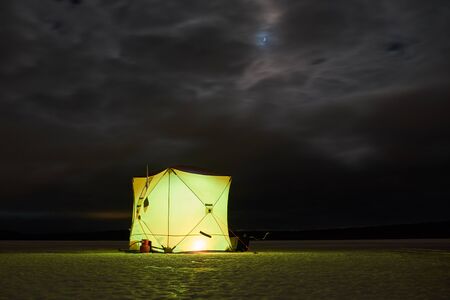 A tent for winter fishing at night stands on a lakeの写真素材