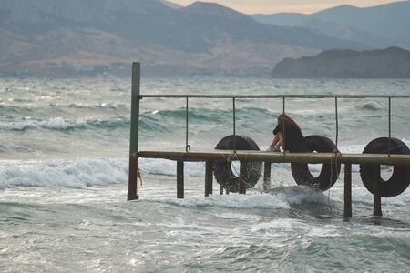 Girl sitting on a pier in the sea.の写真素材