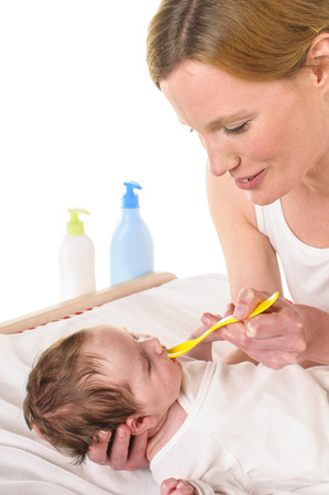 Young mother with her newborn baby infant care operates on the changing table, she gives the baby a drug with a yellow plastic spoon, isolated against a white background の写真素材
