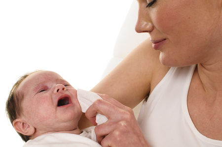 An adult woman with white shirt holding a also dressed in white infant tenderly in her arms and dabbed it with a tissue for cleaning the mouth, isolated against a white background の写真素材