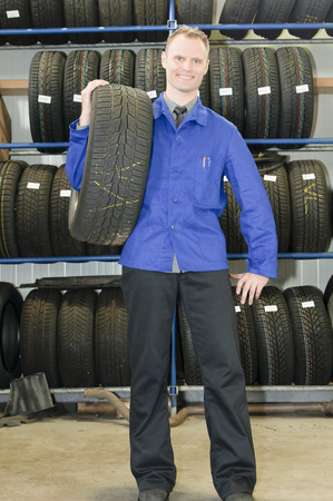 Car mechanic in blue overalls pulls a tire from the tire store in the garageの写真素材