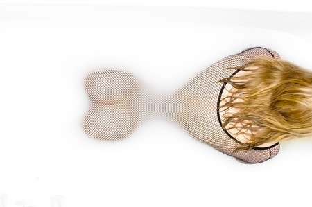 Young woman lying in the Bathtub and wearing a sexy fishnet bodystocking. Showing her backside and her butts.の写真素材