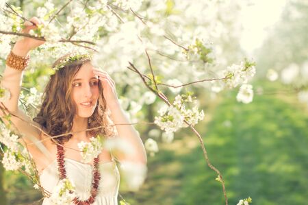 Young woman in white dress standing smiling amide colored blooming cherry trees
