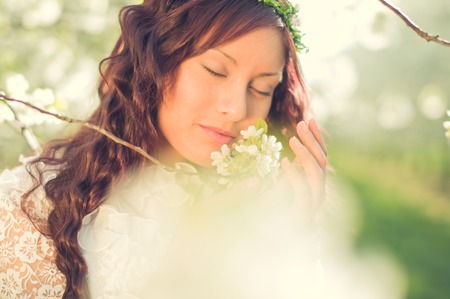 girl hippie is in the middle of white blossoming cherry trees and smells thoughtfully at the flowersの写真素材