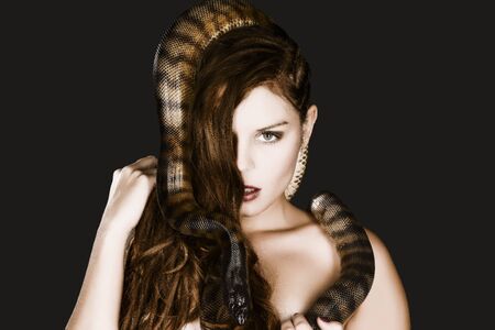 A pretty young woman with brunette hair looks at the camera head to her bare neck snaking a big dark...