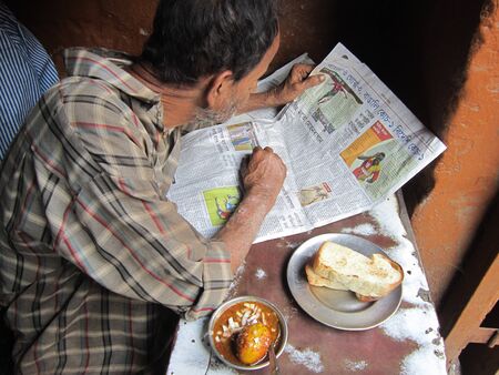 MAN READING NEWSPAPER AND EATING SNACKS.SHOT AT CALCUTTA, INDIA: MORNING HOURS ON NOVEMBER 18,2012.のeditorial素材