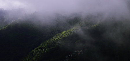mist, monsoon clouds and darkness create dramatic landscape. beautiful mountain village on himalayan foothills near mirik in darjeeling, indiaの写真素材