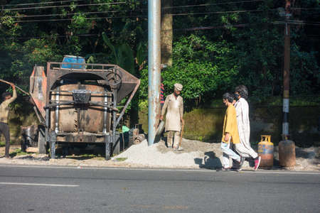 10th october 2021. Dehradun, Uttarakhand, India. A group of construction workers putting raw material inside a mixture machine for asphalt road building.のeditorial素材