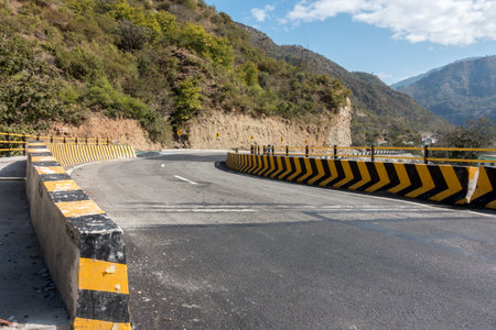 A wide angle shot of an all weather asphalt road with yellow concrete barriers. Uttarakhand, India.