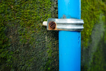 A big blue plastic pipe secured on a weary wall with grouted clips. India.