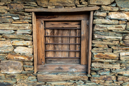 Traditional stone hut in Uttarakhand, India, featuring a wooden window set within a rugged stone...
